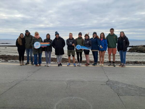 A group of people standing looking at the camera on a beach holding Mental Health Ireland handheld signs
